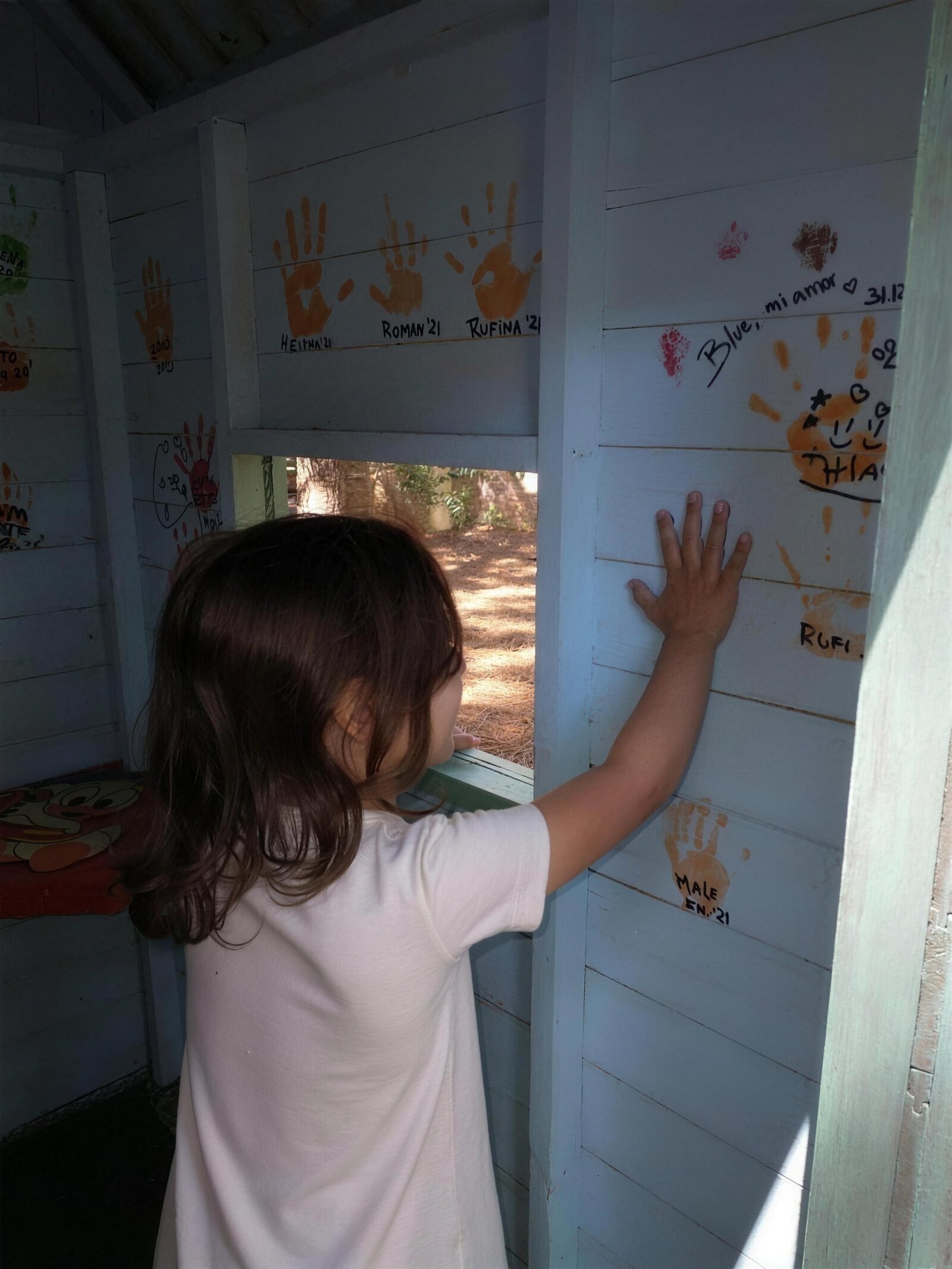 Nena mirando por la ventana de la casita de juegos, con las manitos pintadas de los chicos que ya visitaron el complejo