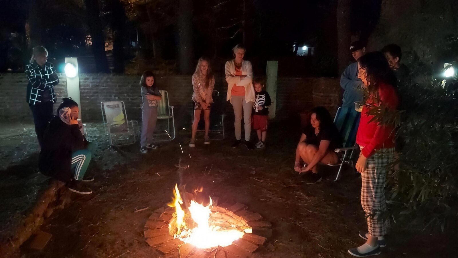 Familias reunidas alrededor del fogón encendido, de noche, bajo los pinos
